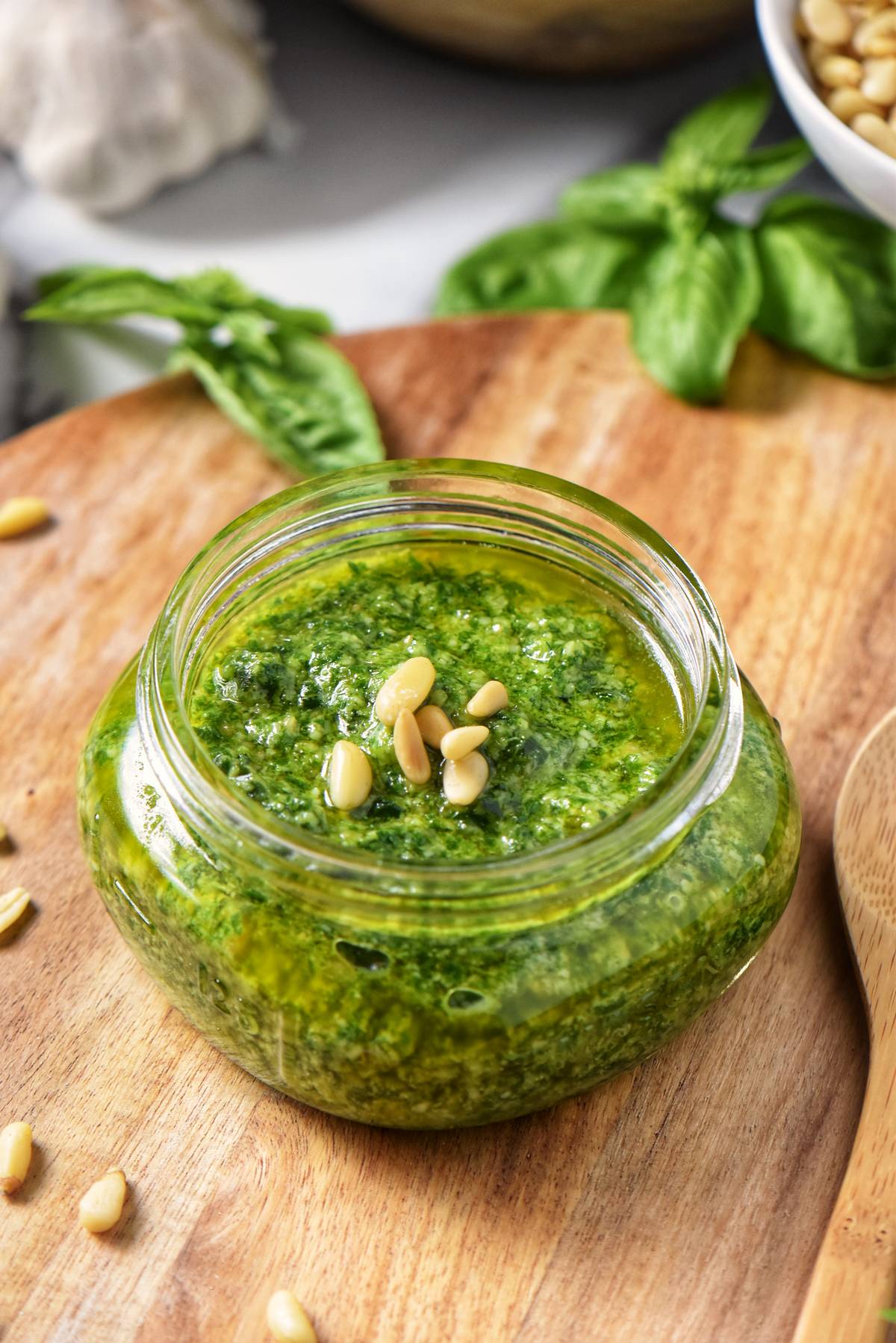 A freshly made jar of basil pesto sauce, topped with a few pine nuts and a layer of olive oil.