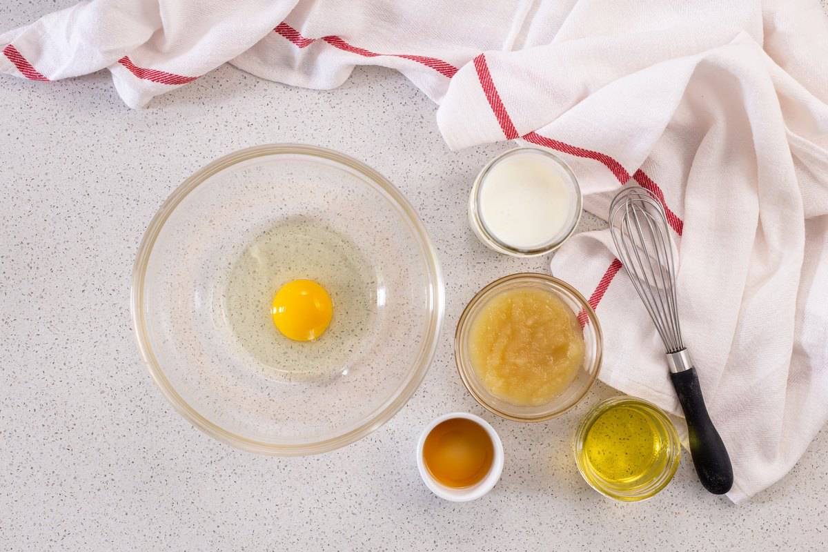 The individual wet ingredients to make the best apple muffins are in several bowls, ready to be whisked together.