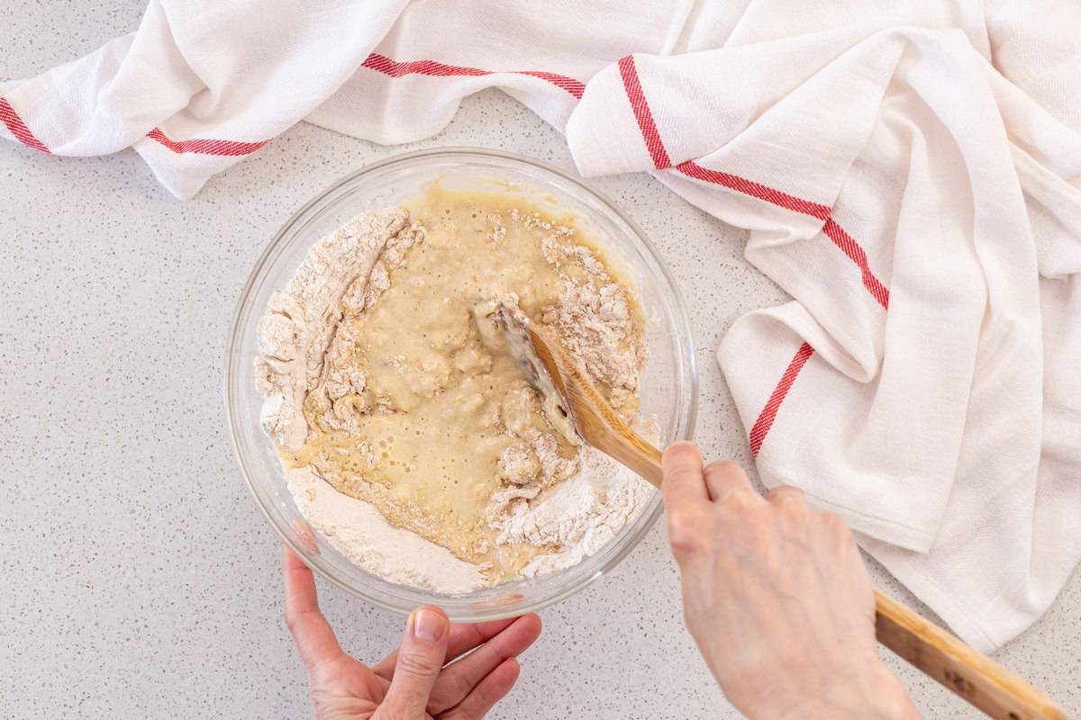 The wet and dry ingredients of an apple muffin recipe combined with a wooden spoon.