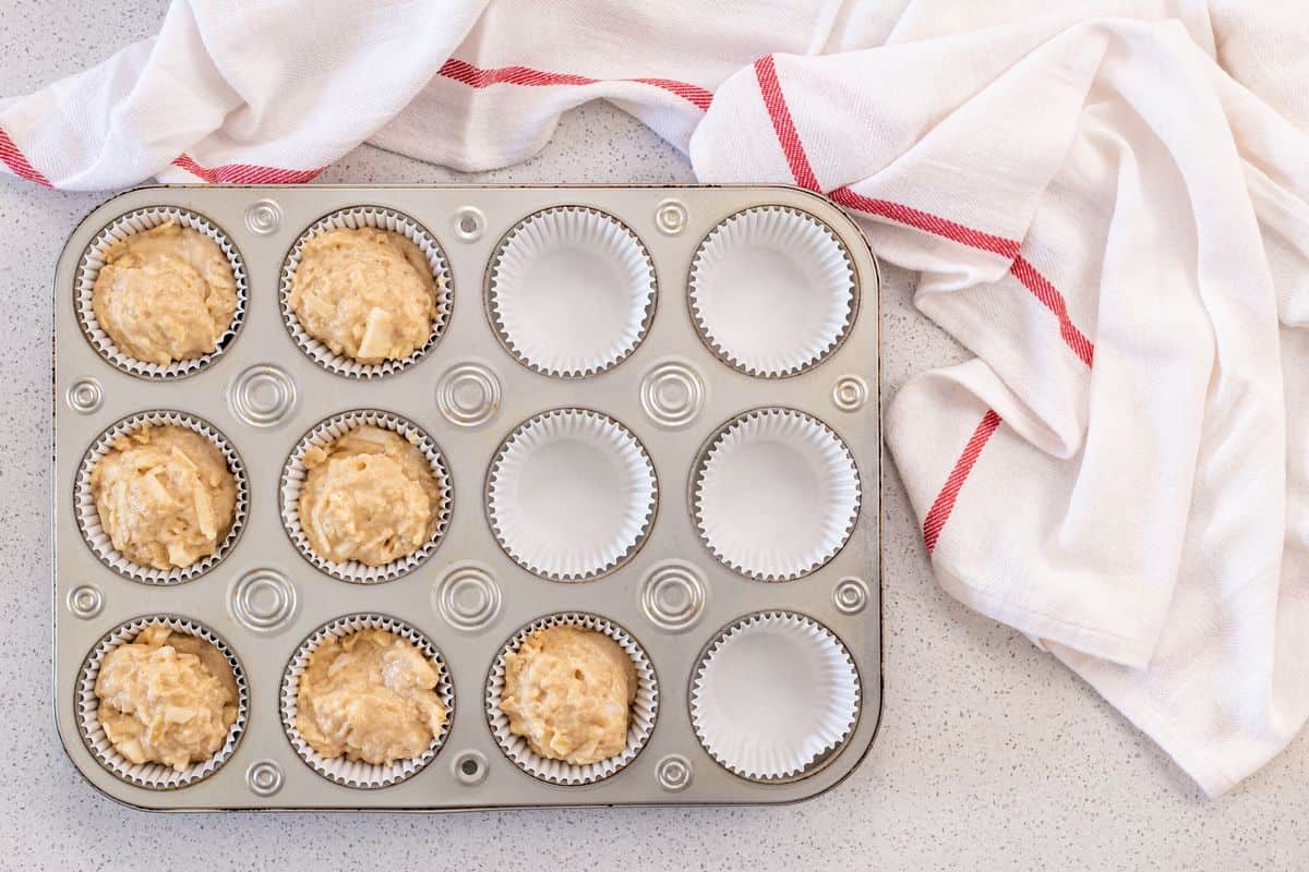 The apple muffin batter is portioned in a muffin pan.