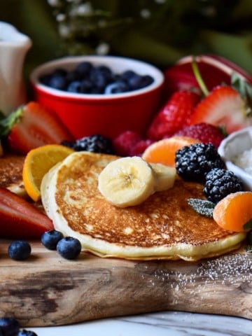 Buttermilk pancakes on a pancake board, surrounded by fruits.