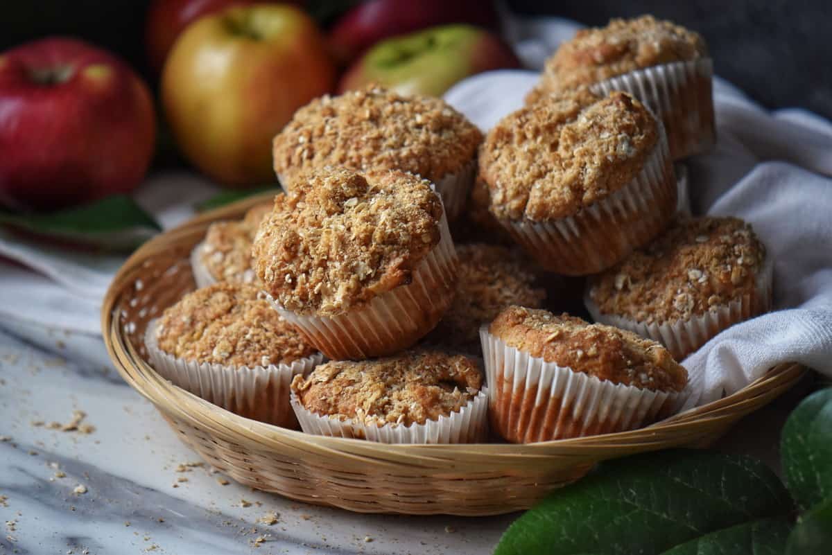 In the foreground, a wicker basket of apple muffins; in the background a few red apples.