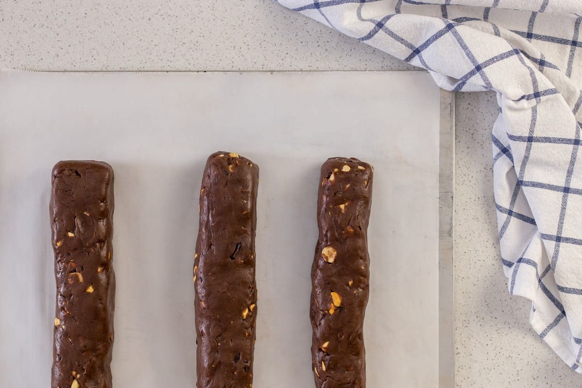 3 chocolate hazelnut logs are placed on a parchment lined baking sheet.