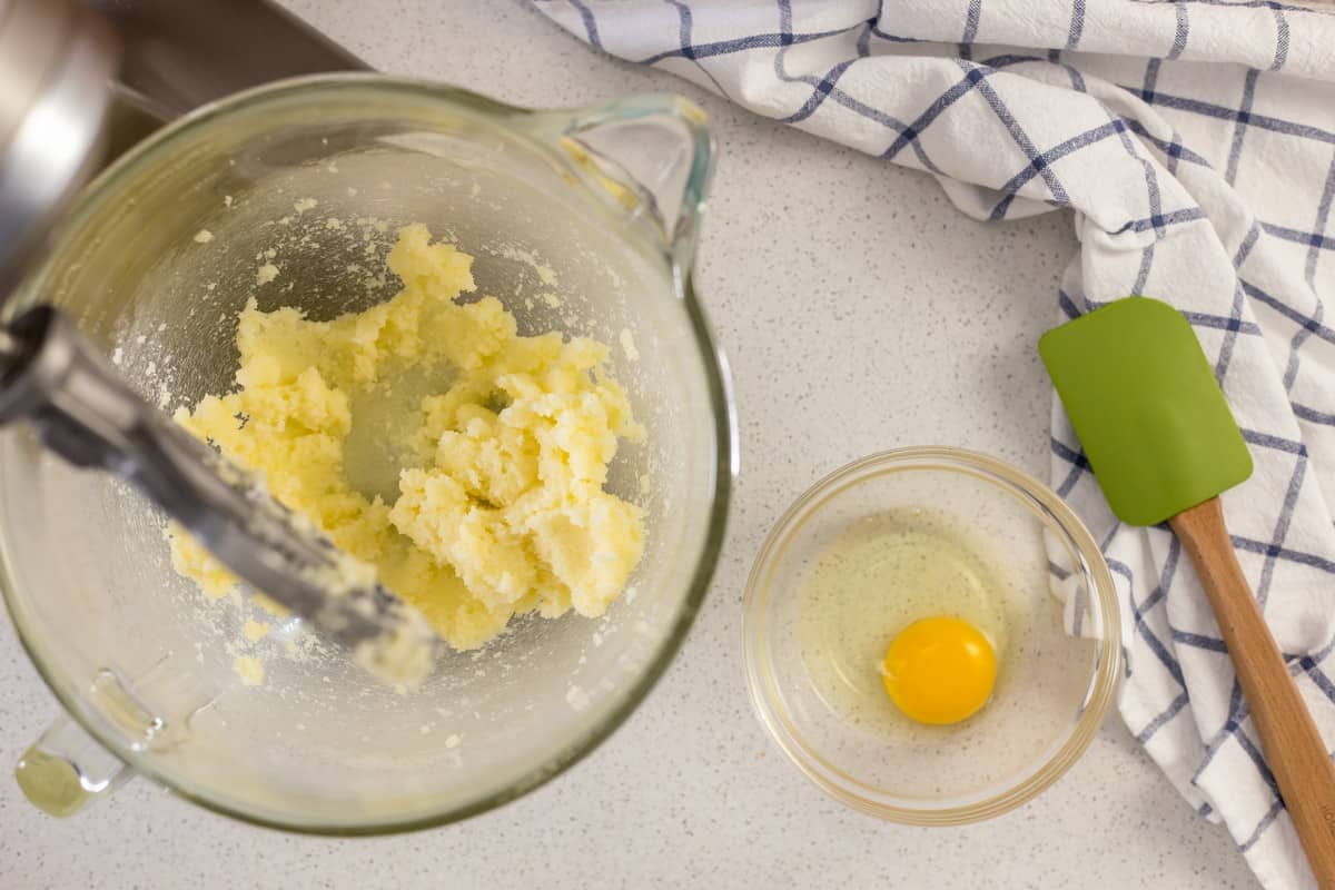 Eggs are in the process of being added to the butter and sugar mixture in the mixing bowl.
