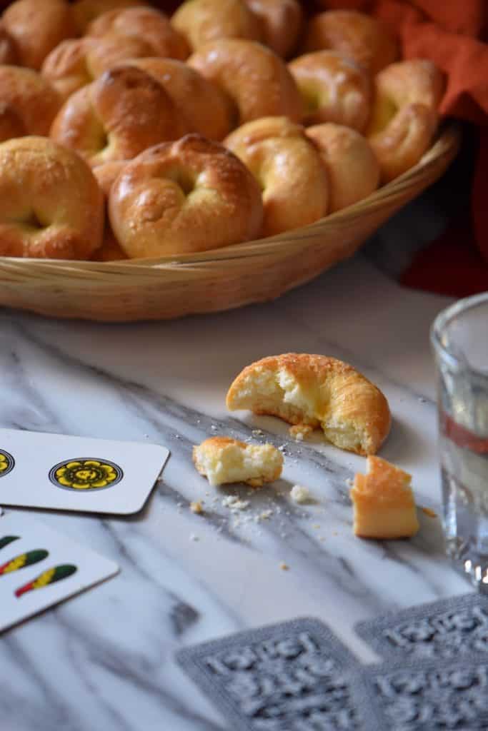 A crumbled Italian wine cookie next to a wicker basket and Italian playing cards.