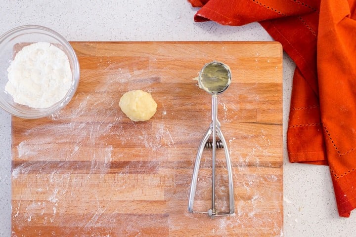 An overhead shot of a scoop of cookie dough on a floured wooden board.