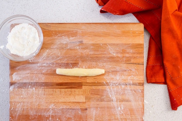 A piece of dough rolled into a log shape on a floured wooden board.