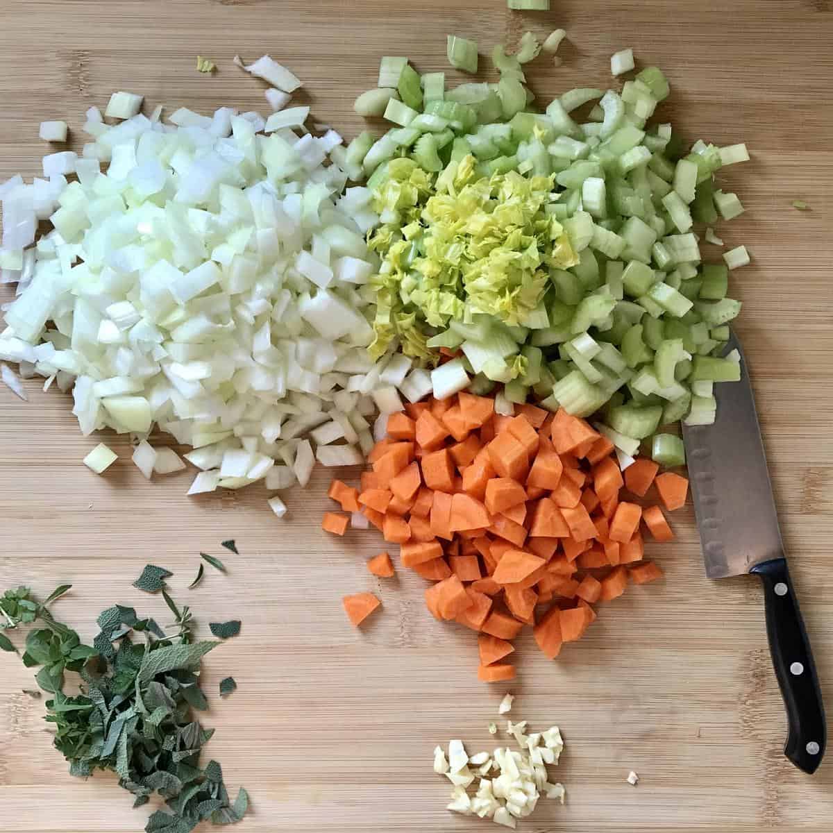 Chopped vegetables and herbs on a wooden board.