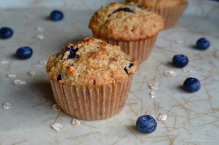 A few Healthy Blueberry Oat Muffins on a tray surrounded by fresh blueberries.