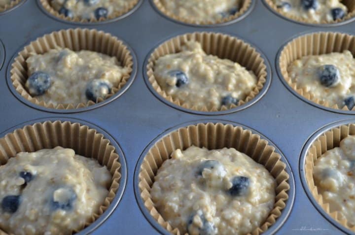 A muffin tin filled with blueberry muffin dough ready to be baked.