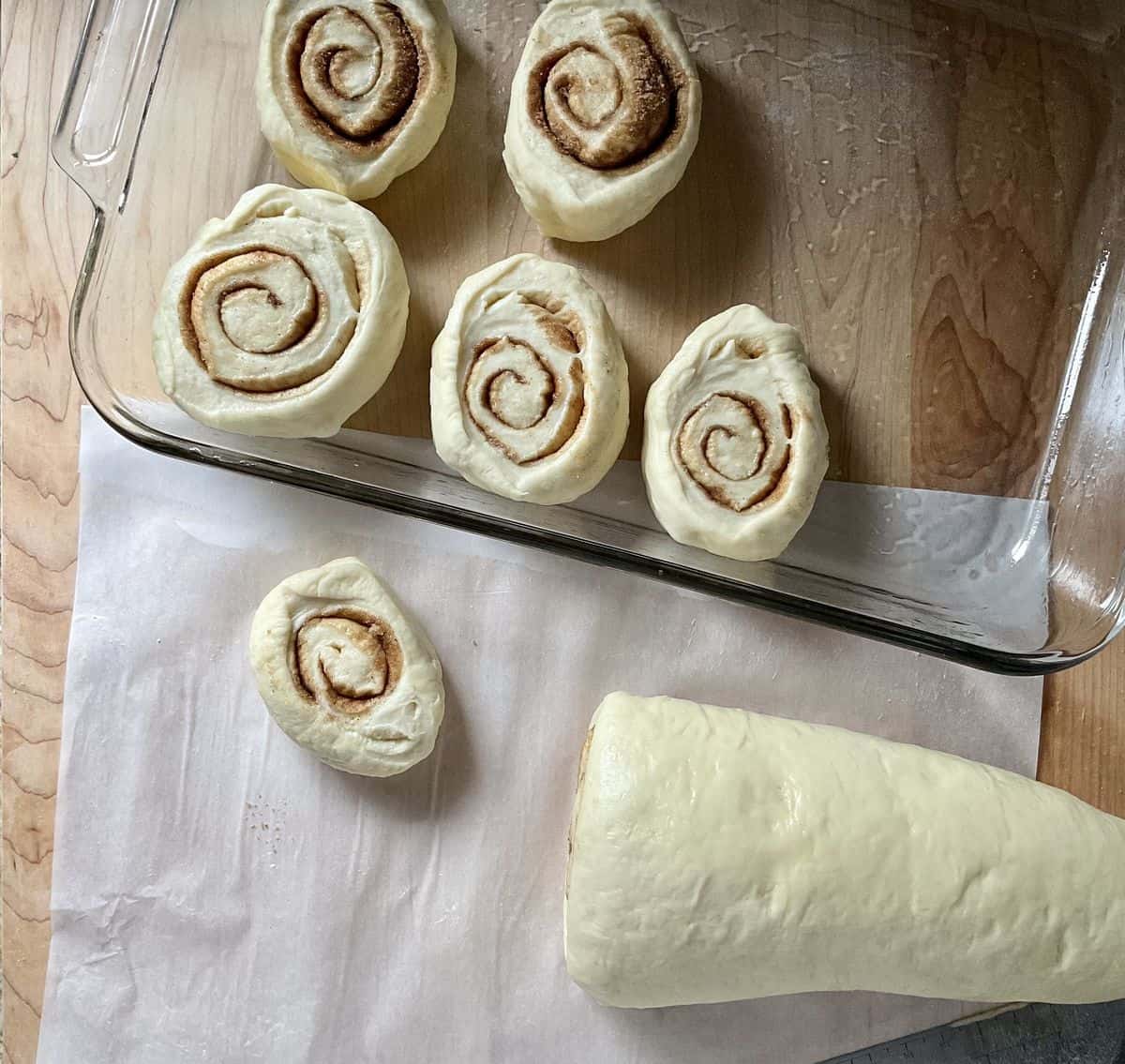 Sliced cinnamon rolls being placed in a greased pan.