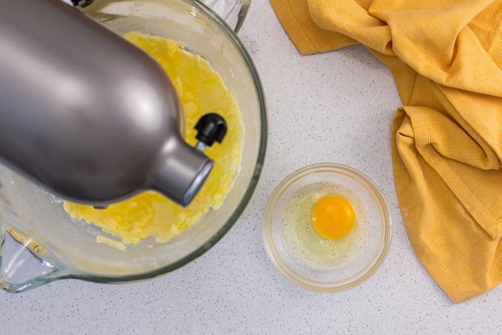 An overhead shot of an egg placed next to a stand mixture.