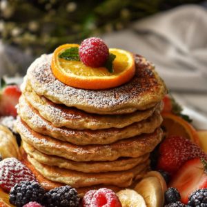 Pancakes surrounded by fresh fruit and dusted with icing sugar.