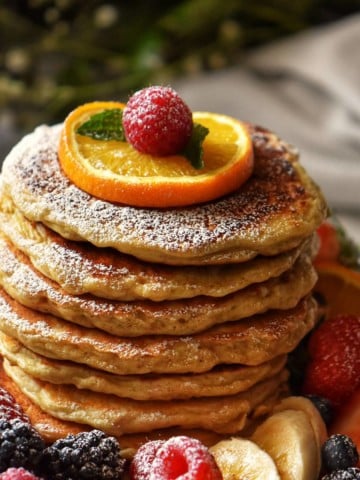 Pancakes surrounded by fresh fruit and dusted with icing sugar.