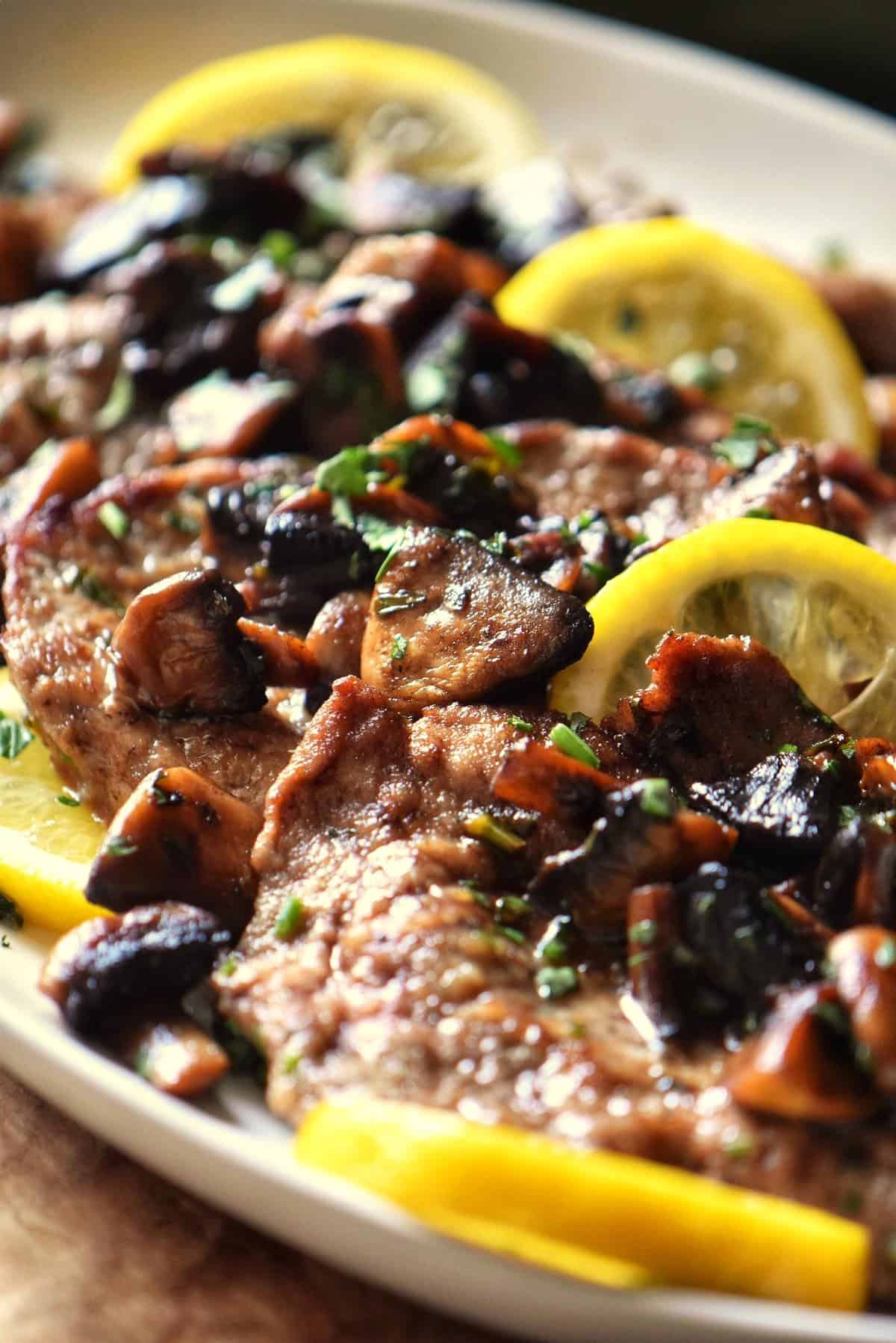 Slices of veal scallopini garnished with Italian parsley and mushrooms.
