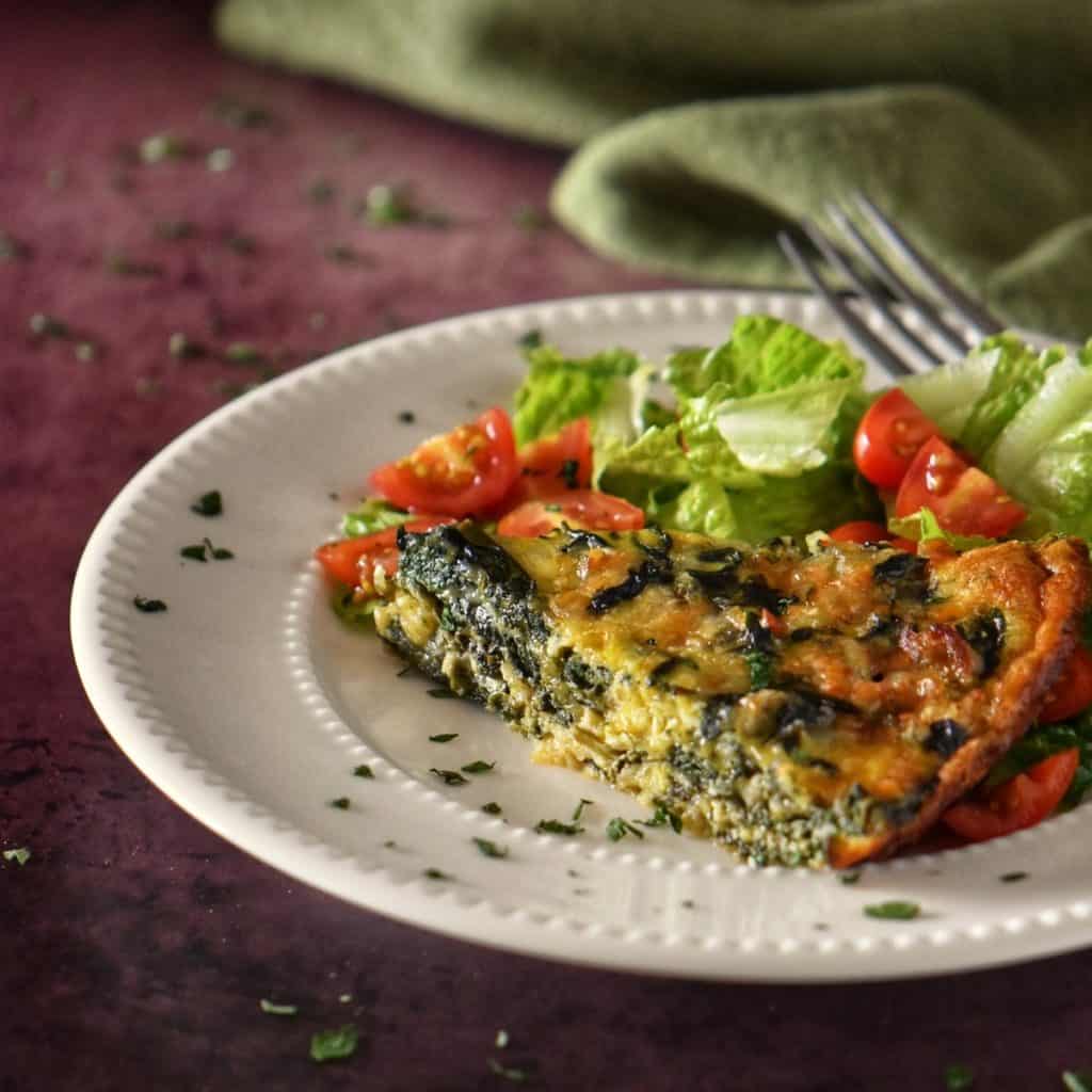 Spinach and cheese quiche next to a salad on a dinner plate.