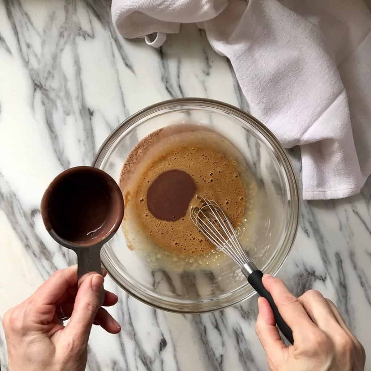 The process of the eggs being tempered with the hot chocolate mixture is being shown.