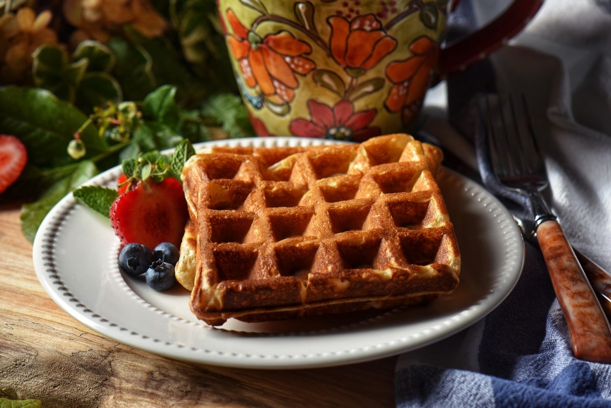 Plain waffles on a white plate with blueberries and strawberries.