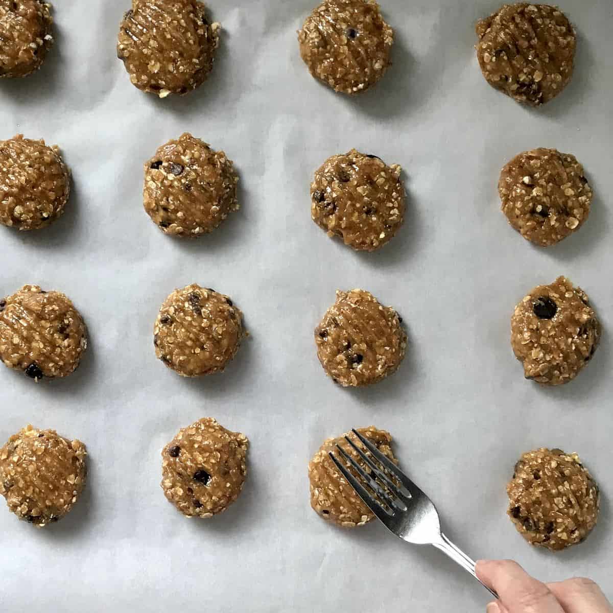  A fork is pressing down on balls of cookie dough.