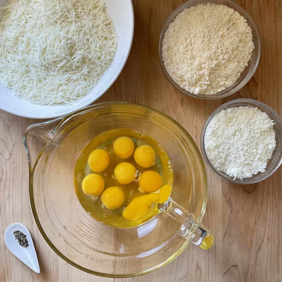 Grated cheese in bowls alongside a bowl of eggs ready to be combined.