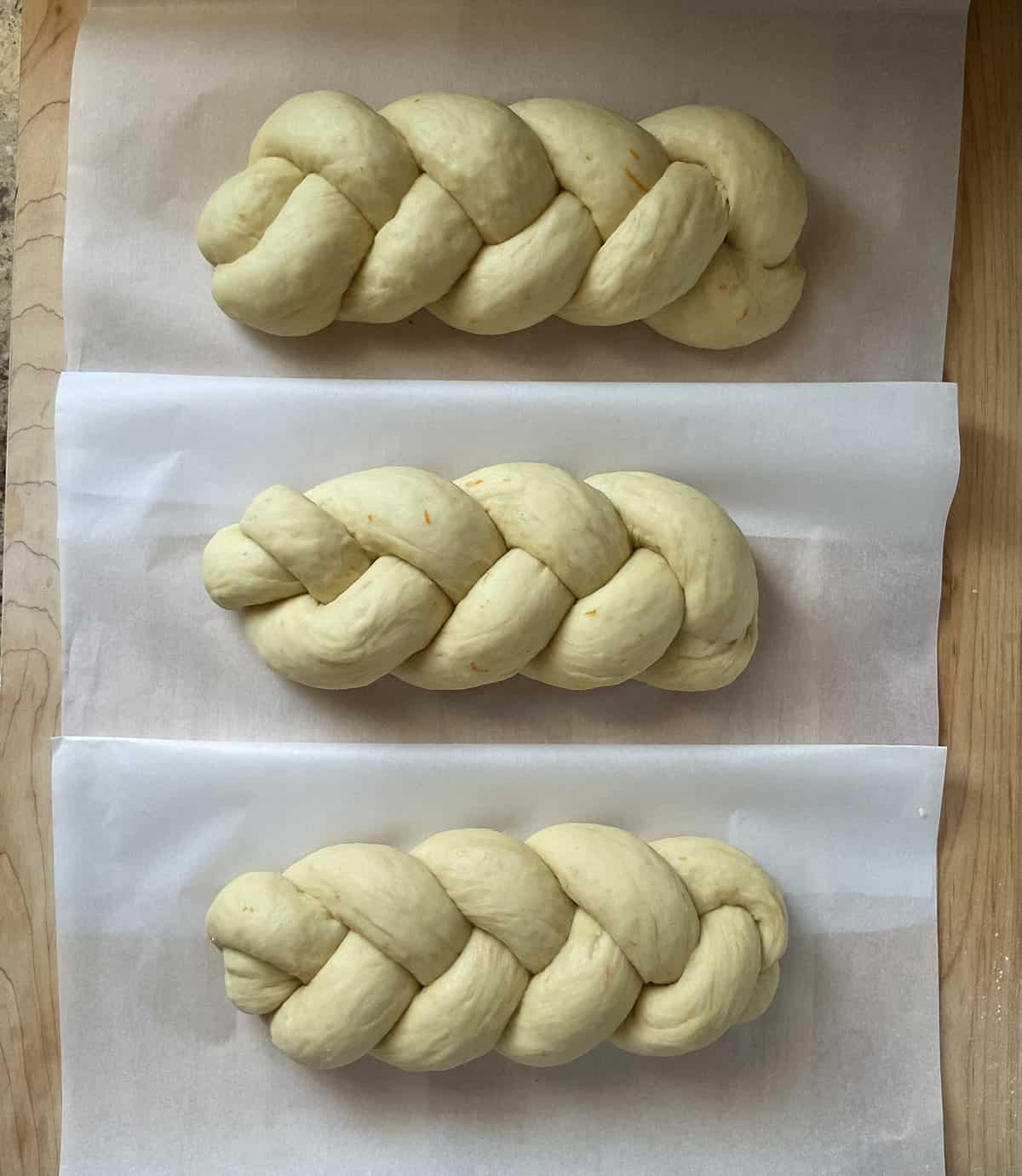 Three braided loaves of Easter bread on a parchment lined baking sheet.