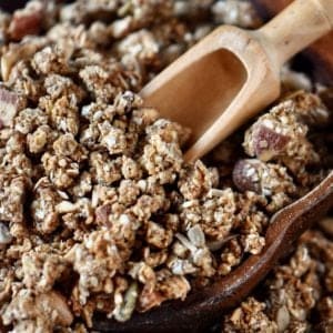 A bowl of crunchy homemade granola with a small wooden scoop.