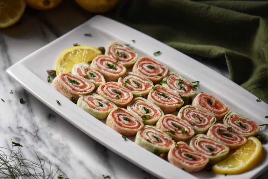 Slices of smoked salmon roll ups on a white serving dish.