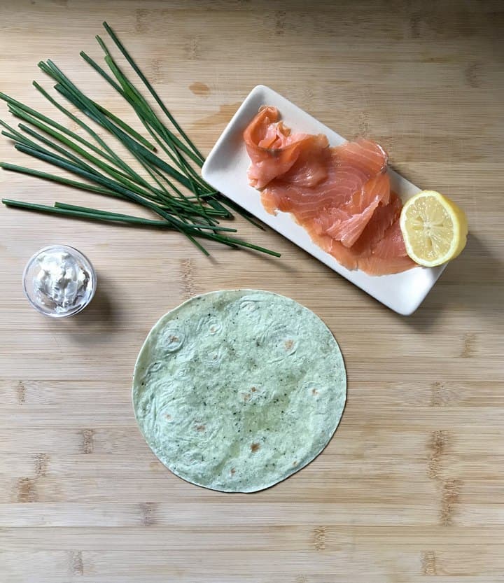 The ingredients to make salmon pinwheels are on a wooden board.