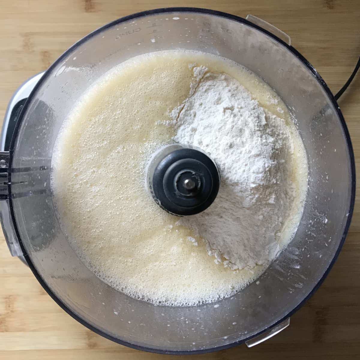 All purpose flour added to the liquid ingredients of a sweet crepe recipe in a food processor.