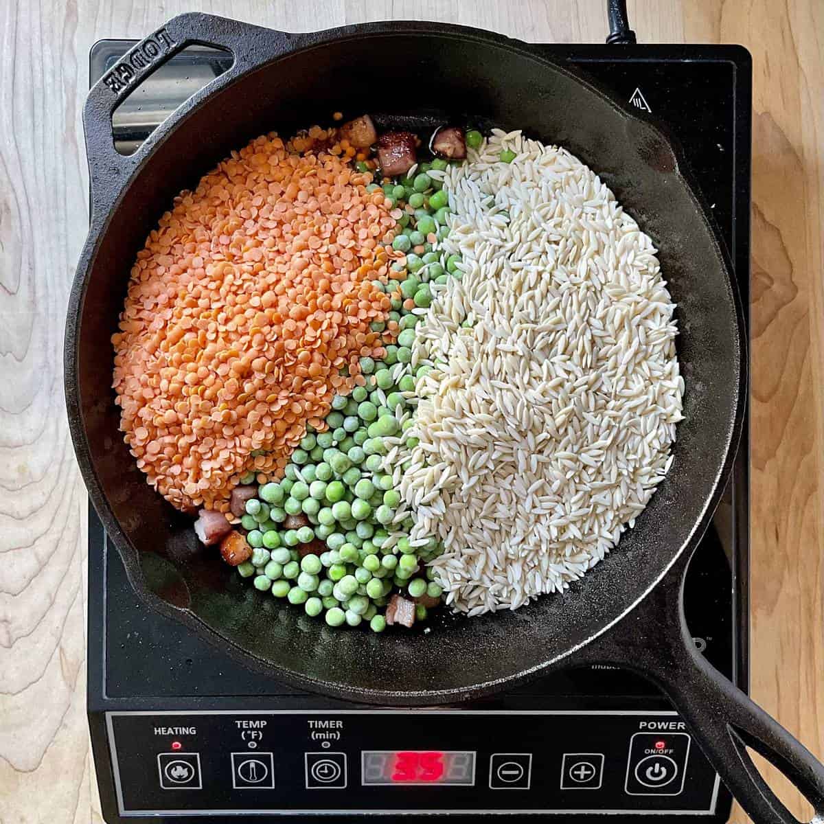 Red lentils, frozen peas and orzo pasta added to pancetta in a cast iron pan.