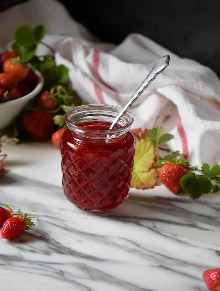 A jar of homemade strawberry jam surrounded by fresh strawberries