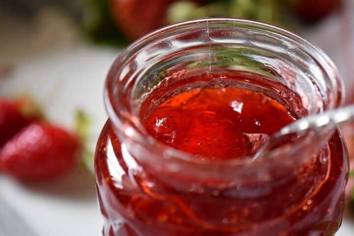A close up of a spoon dipped in a jar of strawberry jam.