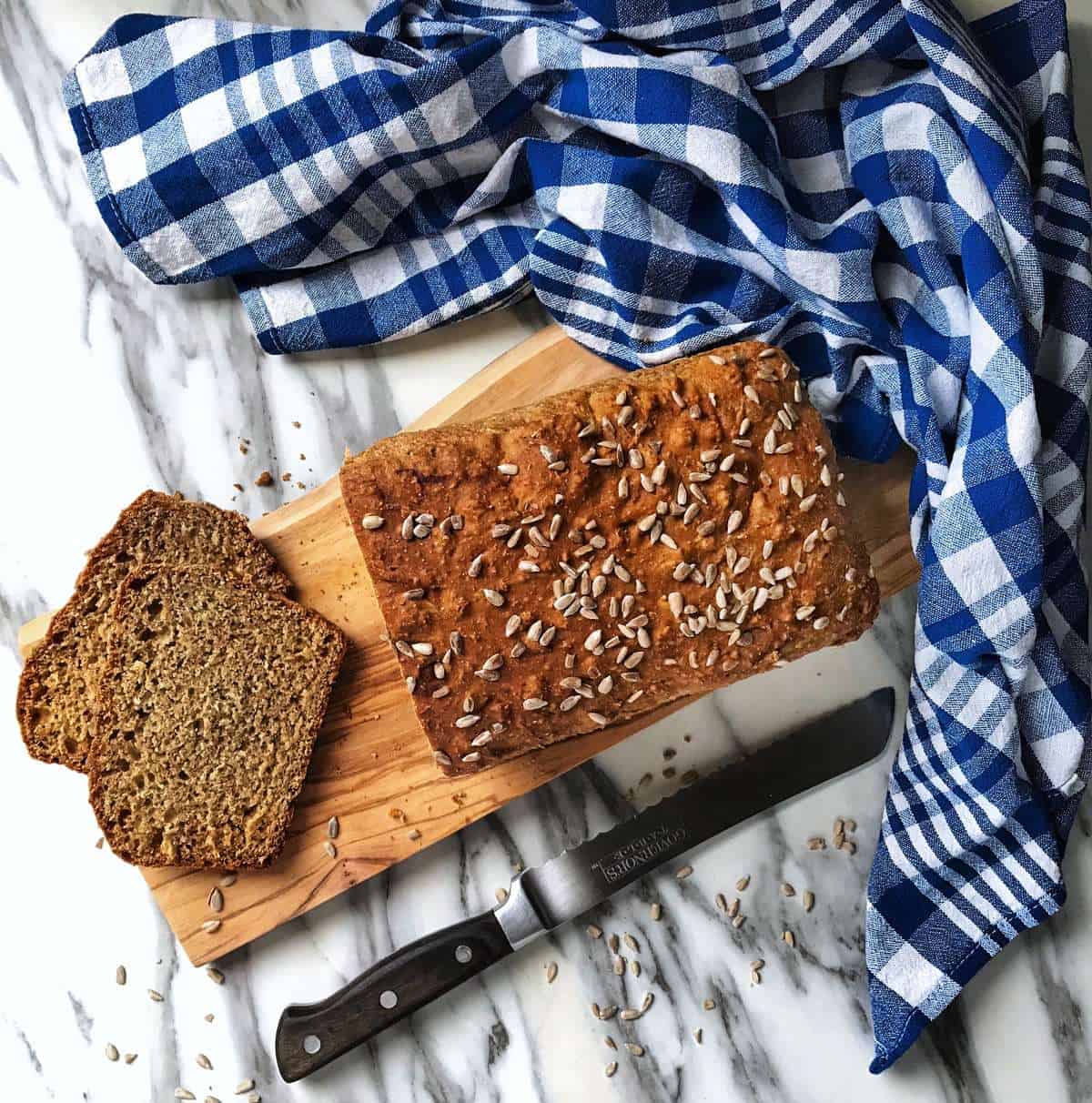 An overhead shot of sliced honey bread with a checkered blue tea towel and a bread knife.