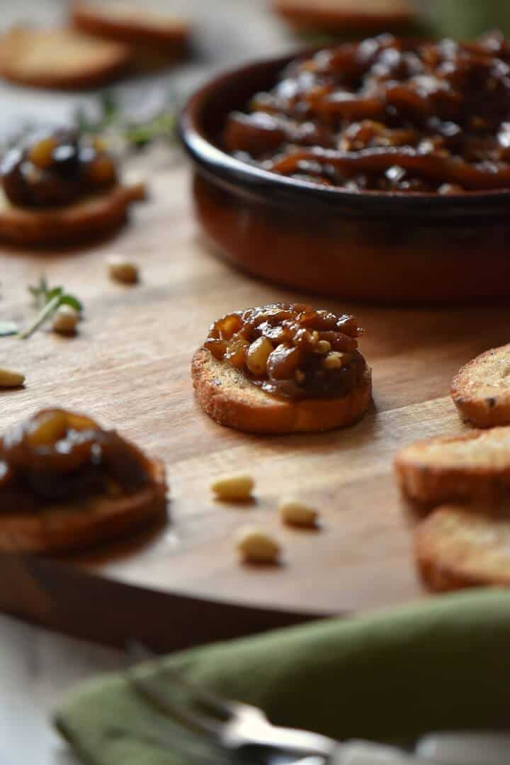 A small round dish of roasted eggplant caponata can be seen in the background; in the foreground, the caponata is placed on a toasted baguette.