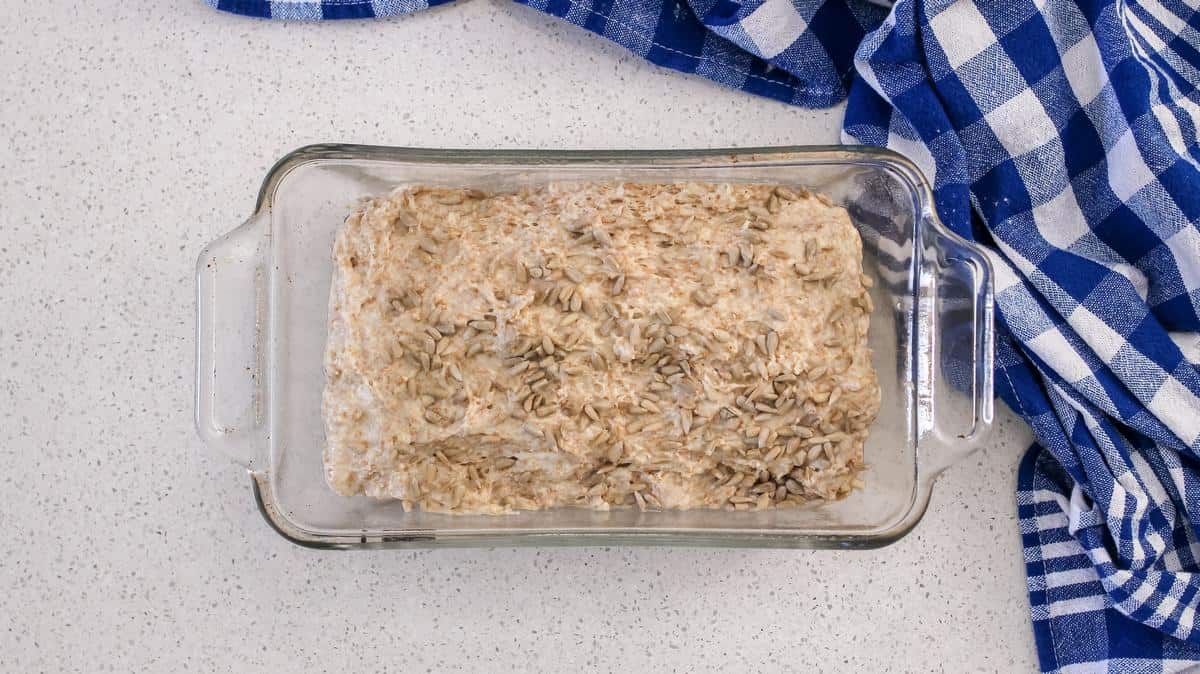 Sunflower seeds can be seen on the honey bread dough in a rectangular pan, about to be baked.