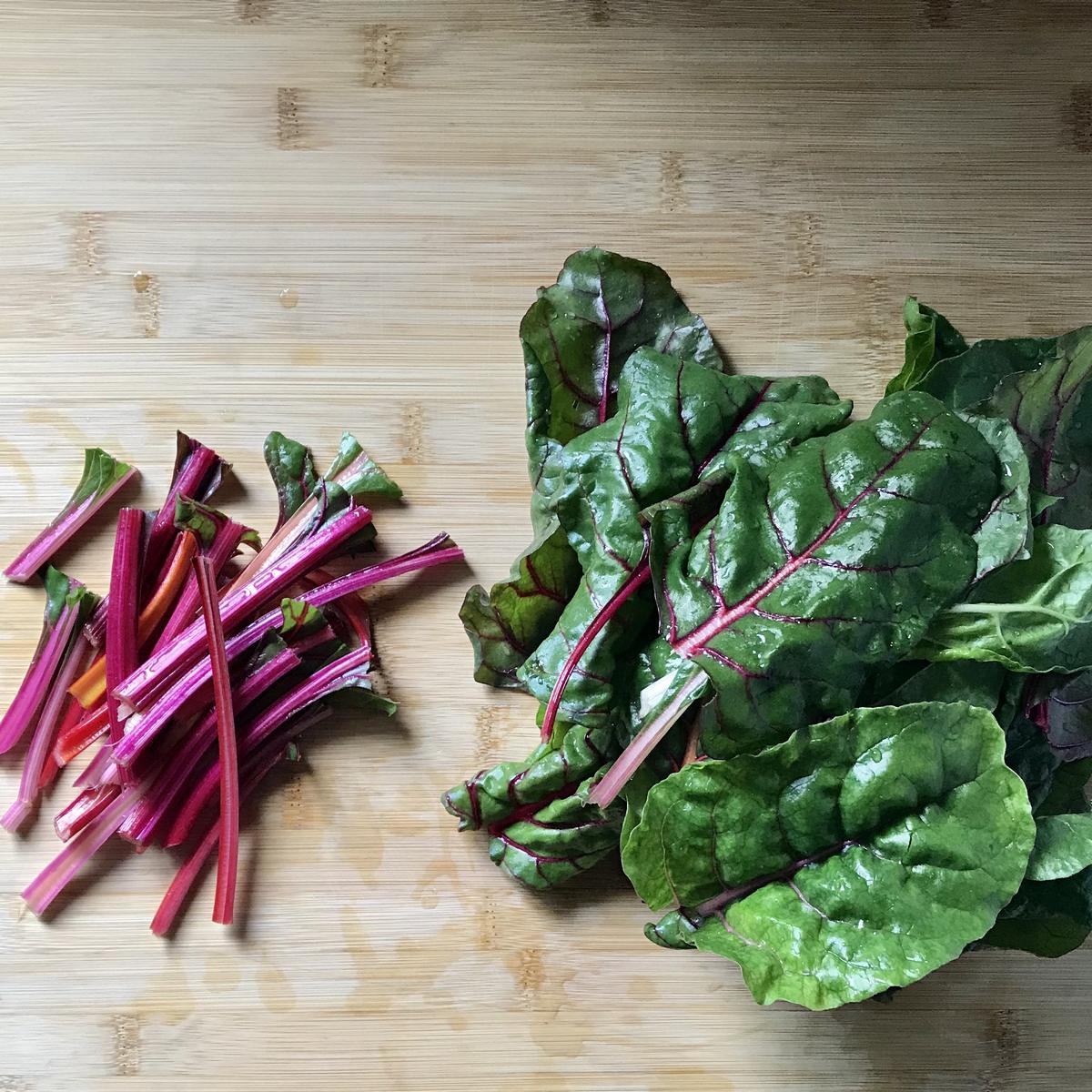 The stems and leaves of rainbow Swiss chard on a wooden board.