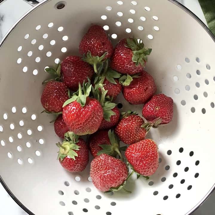 Strawberries in a white colander about to be rinsed.