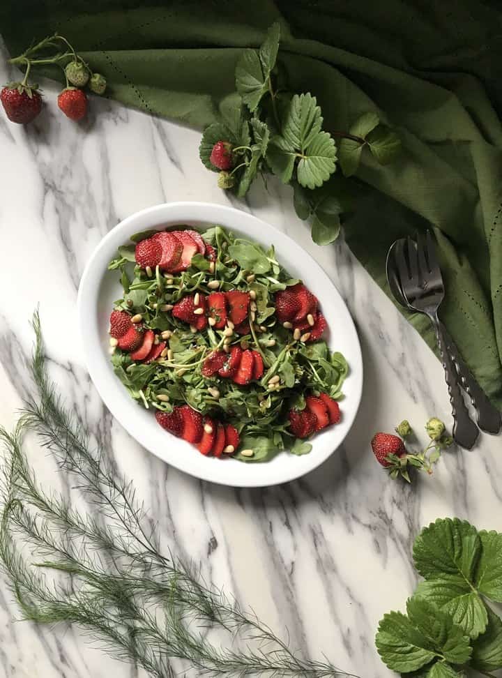 A large white platter of strawberry arugula salad.