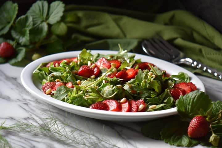 A white oval platter filled with a colorful arugula salad.