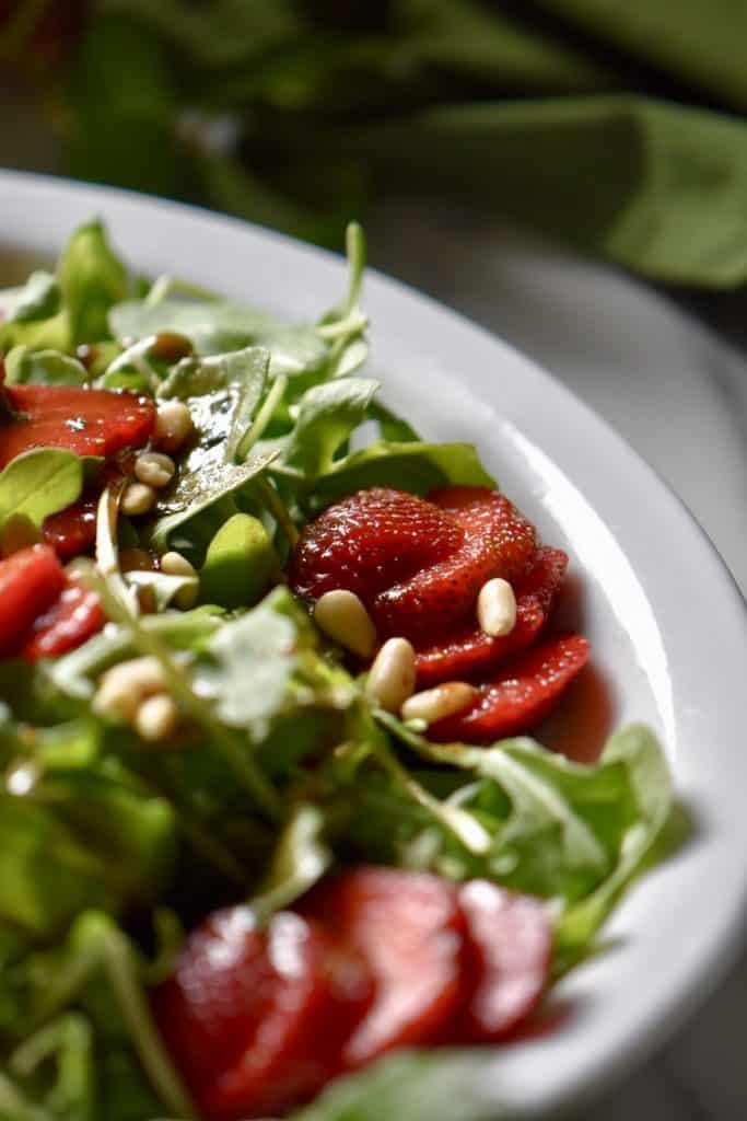 A summer salad with arugula and strawberries in a white oval dish. 