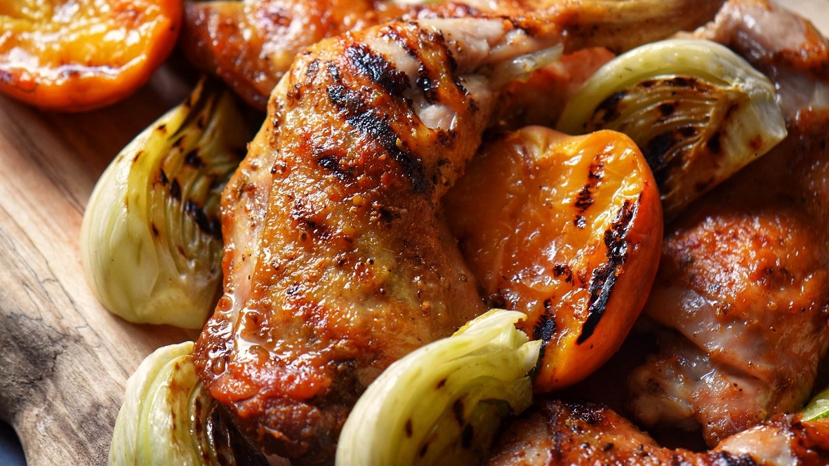 A grilled chicken leg quarter next to grilled fennel and peaches.
