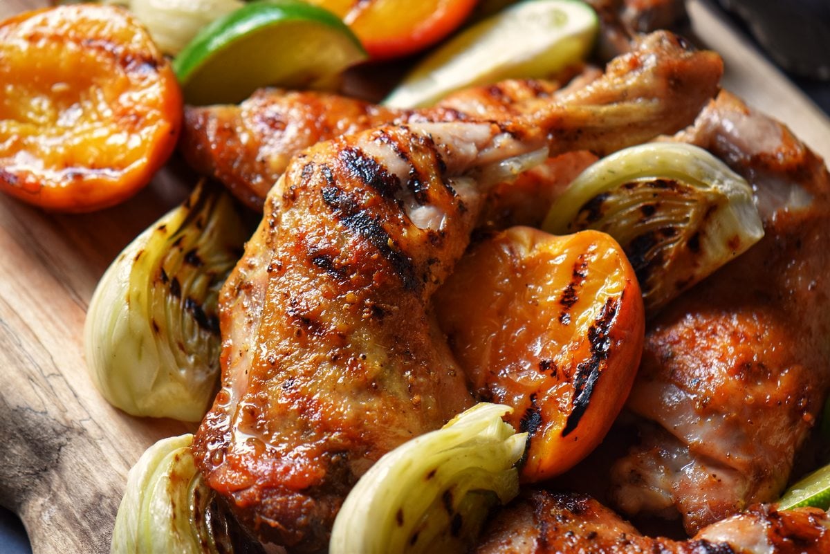 Grilled chicken quarters, fennel and peaches on a wooden board. 