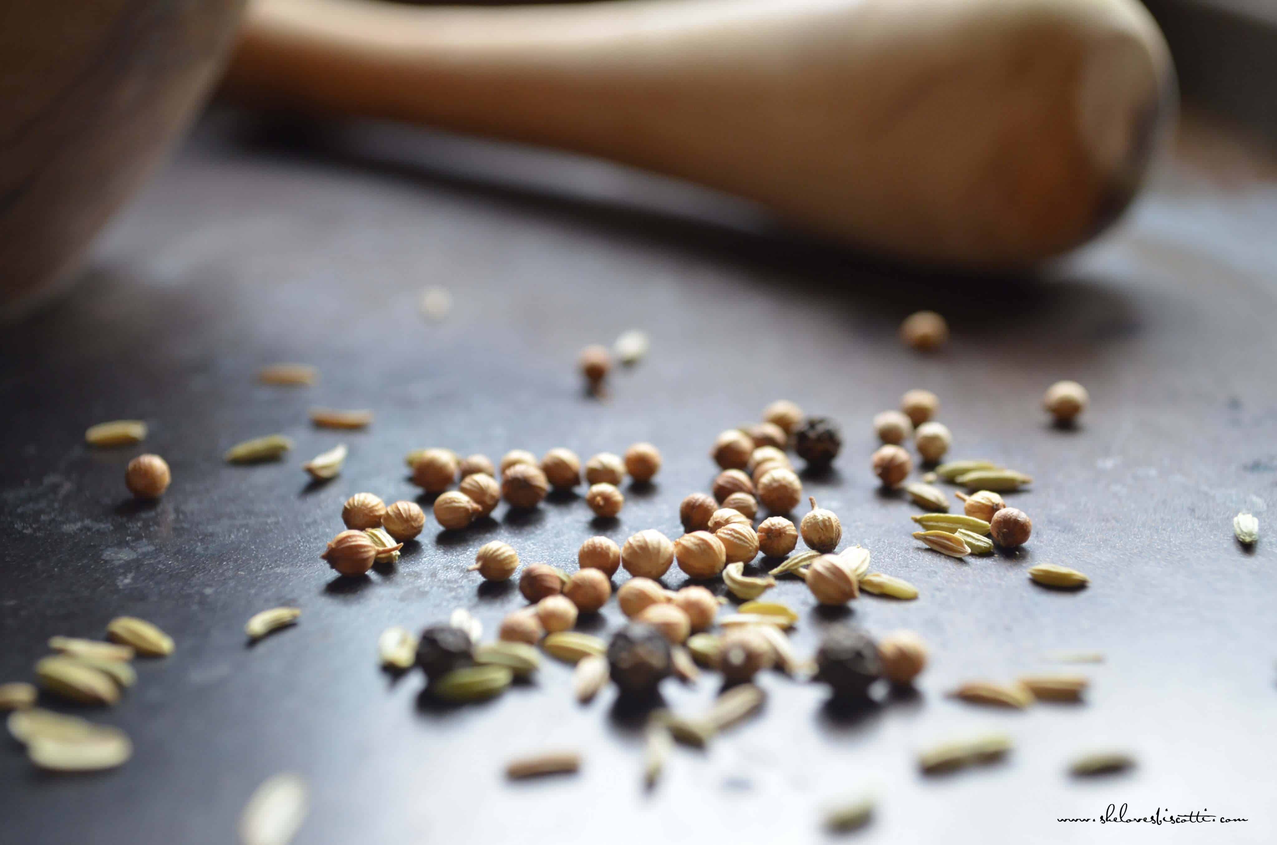 Fennel seeds, coriander and peppercorns next to a mortar and pestle.