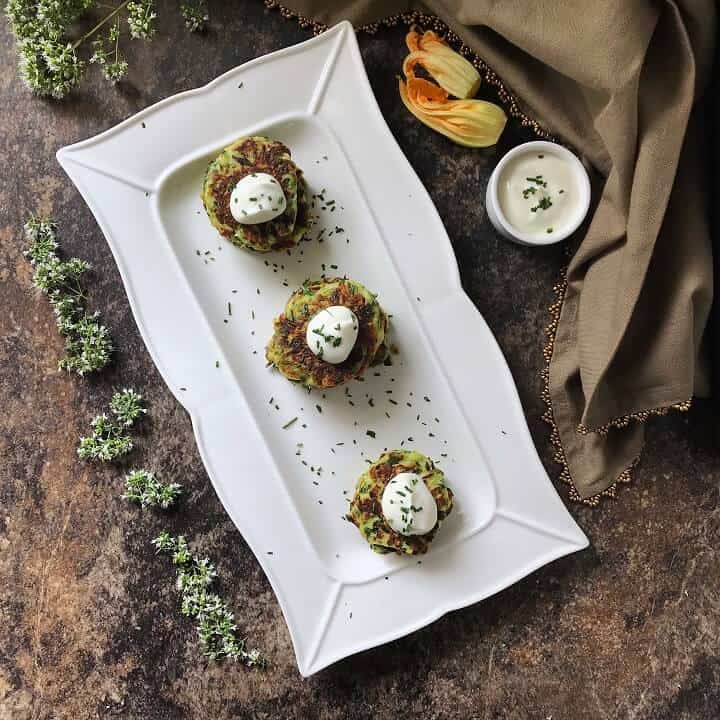 An overhead shot of zucchini fritters on a white plate served with a dollop of yogurt sauce.