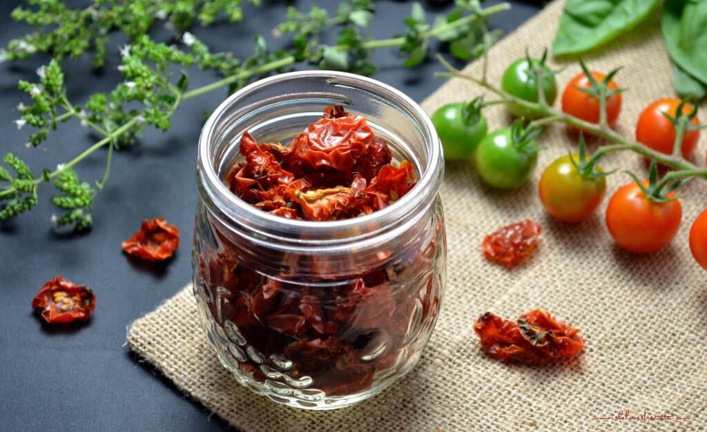 Scattered oven dried cherry tomatoes surround a mason jar filled with more dehydrated cherry tomatoes.