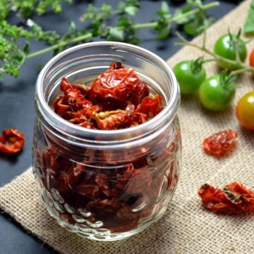Scattered oven dried cherry tomatoes surround a mason jar filled with more dehydrated cherry tomatoes.