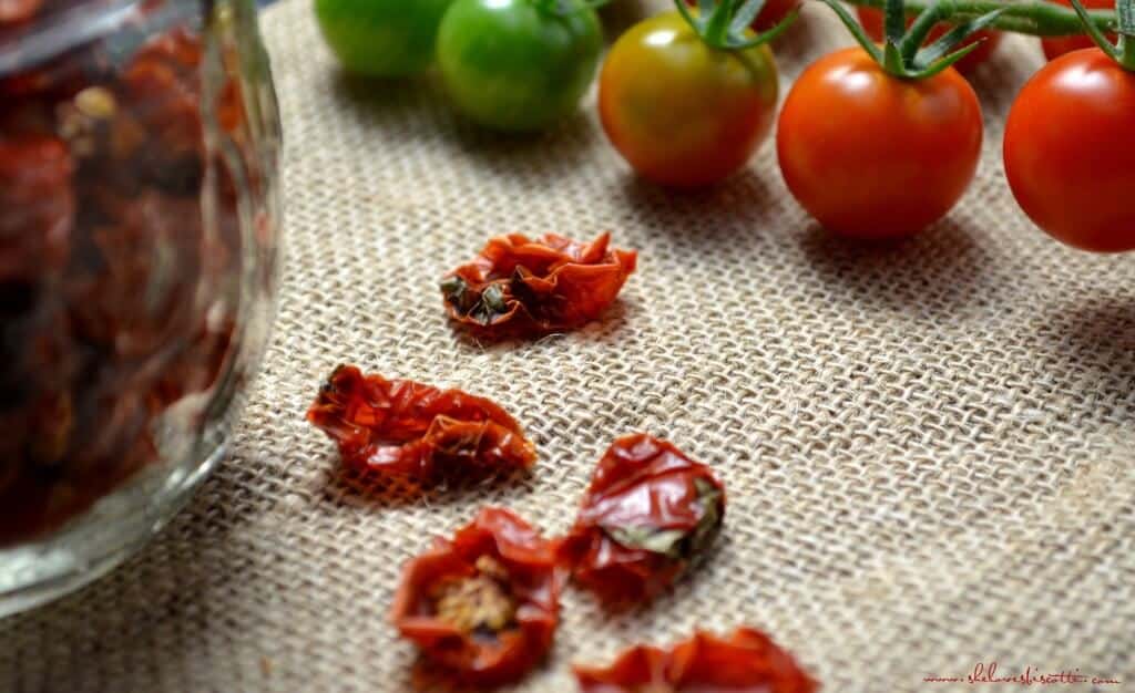 A close up shot of sun dried cherry tomatoes. In the background, fresh cherry tomatoes can be seen.