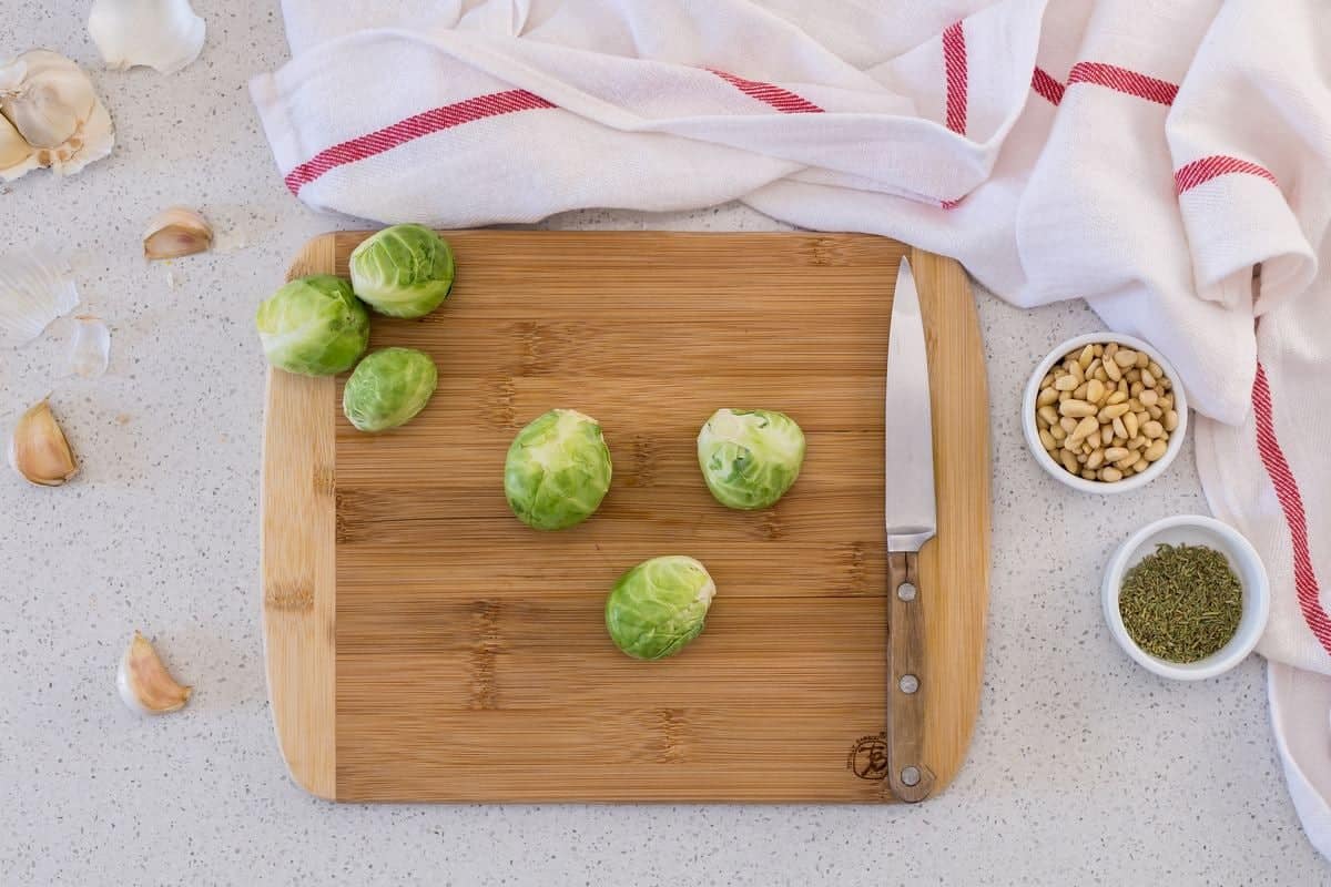 Brussels sprouts on a wooden board about to be sliced in half with a knife.