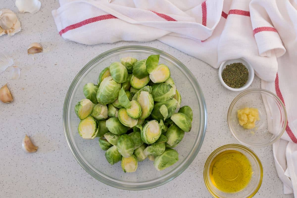 Brussels sprouts in a bowl surrounded by olive oil, garlic and rosemary.