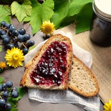 An overhead shot of the purple concord grape jelly spread over a slice of whole wheat bread.